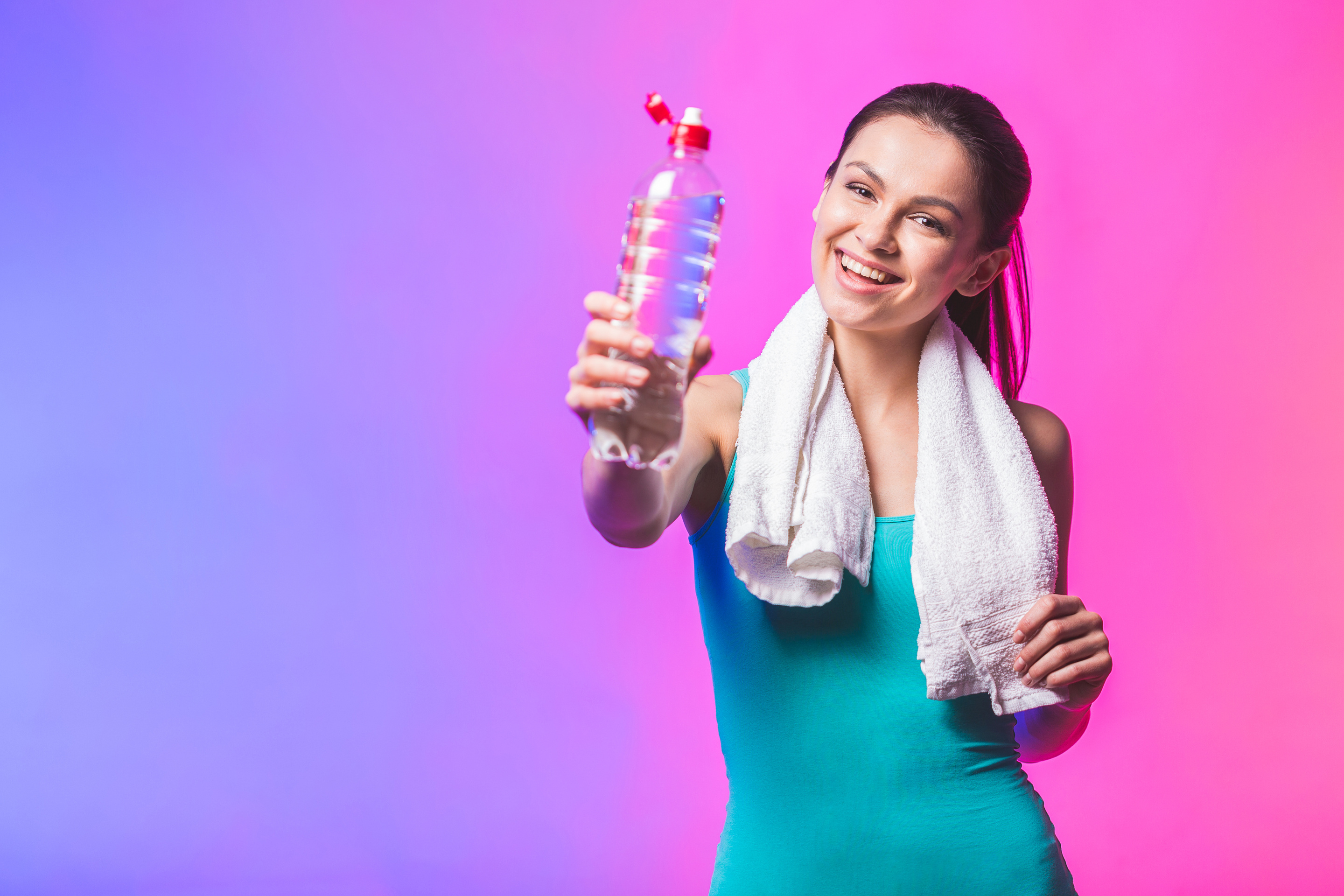 Resting time. Sporty girl with bottle of water and towel on her shoulders. Photo of fitness model isolated on white background. Sport and healthy lifestyle.